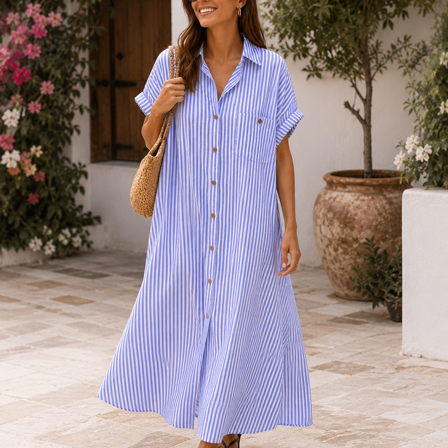 A woman wearing a light blue and white vertically striped midi shirt dress with short sleeves, a button-down front, and a small chest pocket, walking outdoors in a sunlit courtyard. She is also wearing sunglasses, a woven shoulder bag, and black sandals.