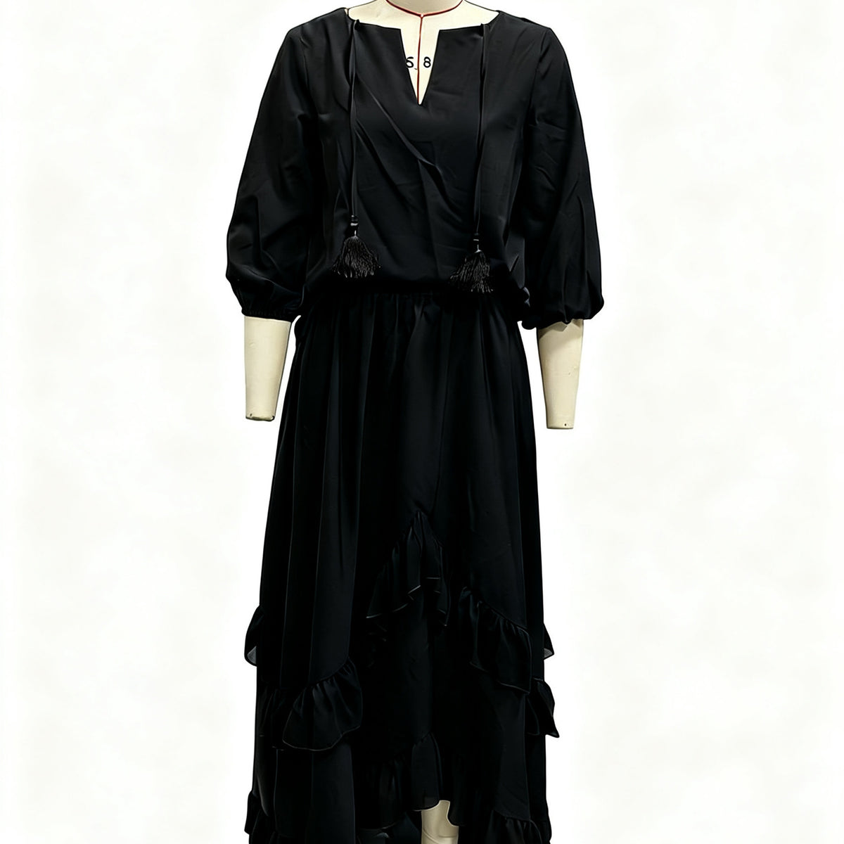A black long-sleeve maxi dress with a wrap-style V-neckline, tassel tie details, and a tiered ruffled hem, displayed on a cream-colored dress form mannequin against a white background.