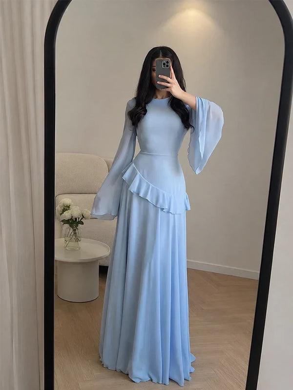 Woman wearing a light blue dress with long sleeves and a peplum waist, standing in front of a mirror.