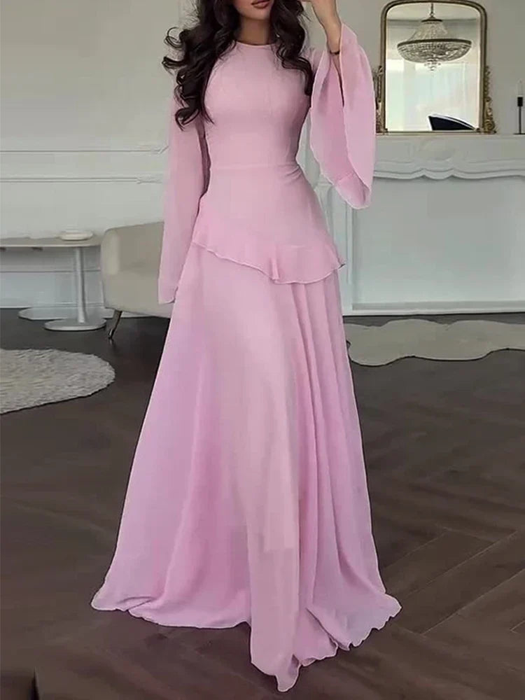 Woman wearing a pink dress in an elegant room with a mirror and chandelier.