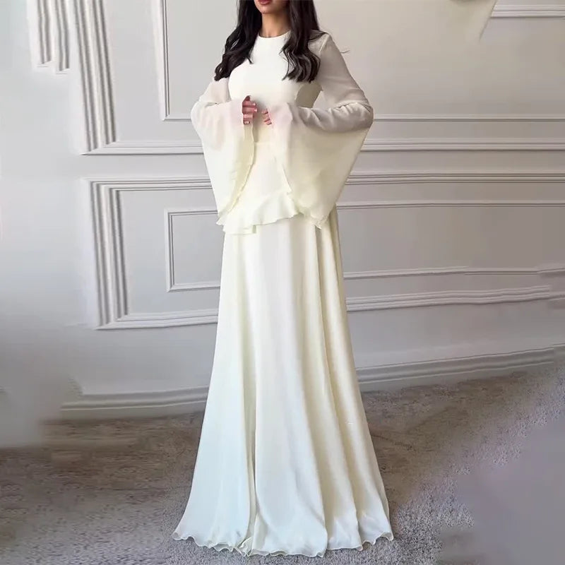 Woman wearing a long white dress with a matching jacket in a room with decorative walls.