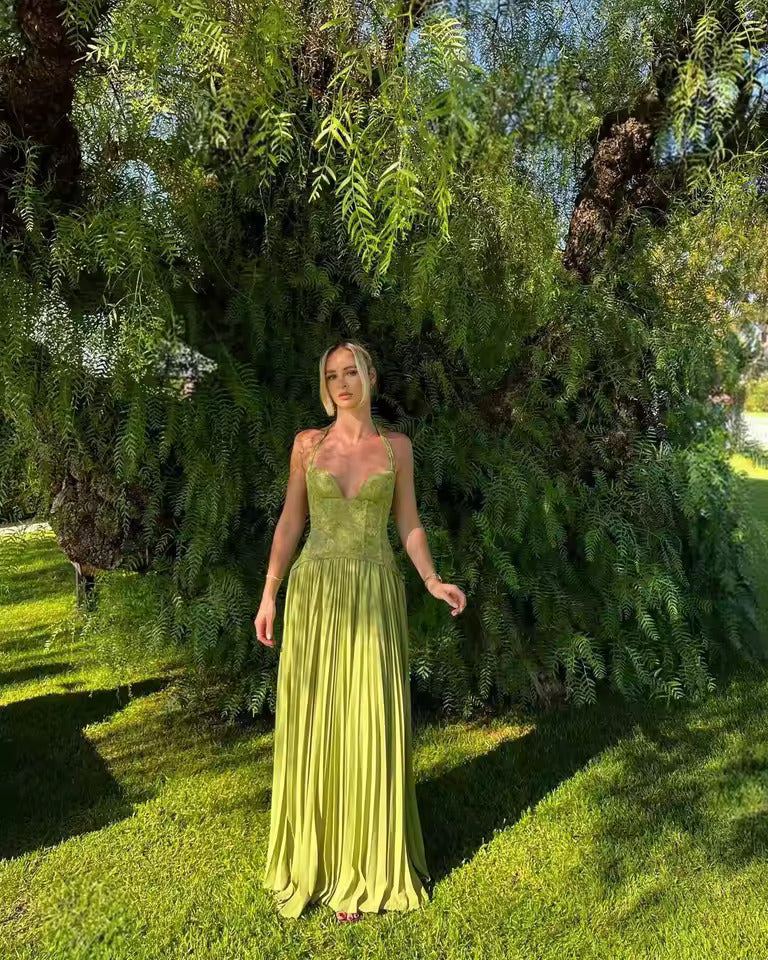 Woman in a green dress standing in a garden with trees and grass.
