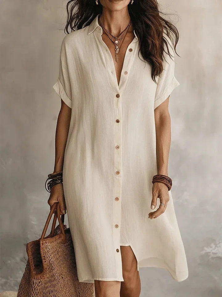 Woman wearing a white button-up dress holding a woven bag against a neutral background