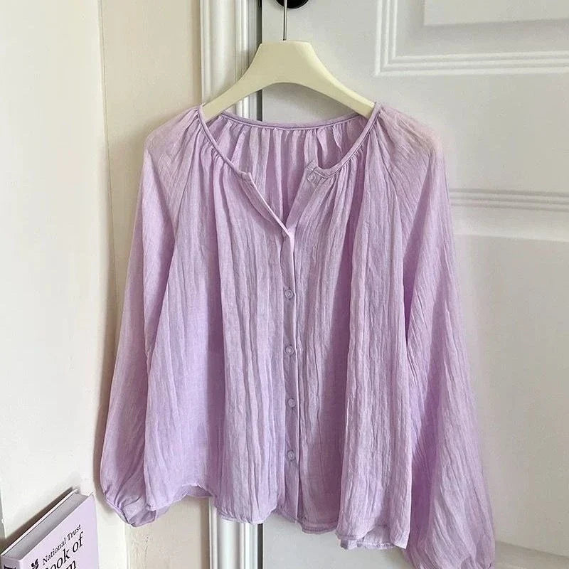 A light purple crinkled cotton blouse with a split V-neckline and button front, hanging on a cream hanger against a white paneled door.