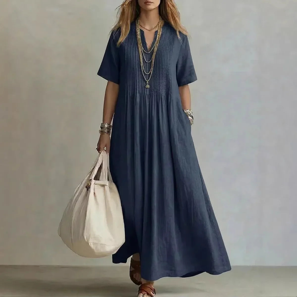 Woman wearing a long blue dress holding a white bag against a neutral background