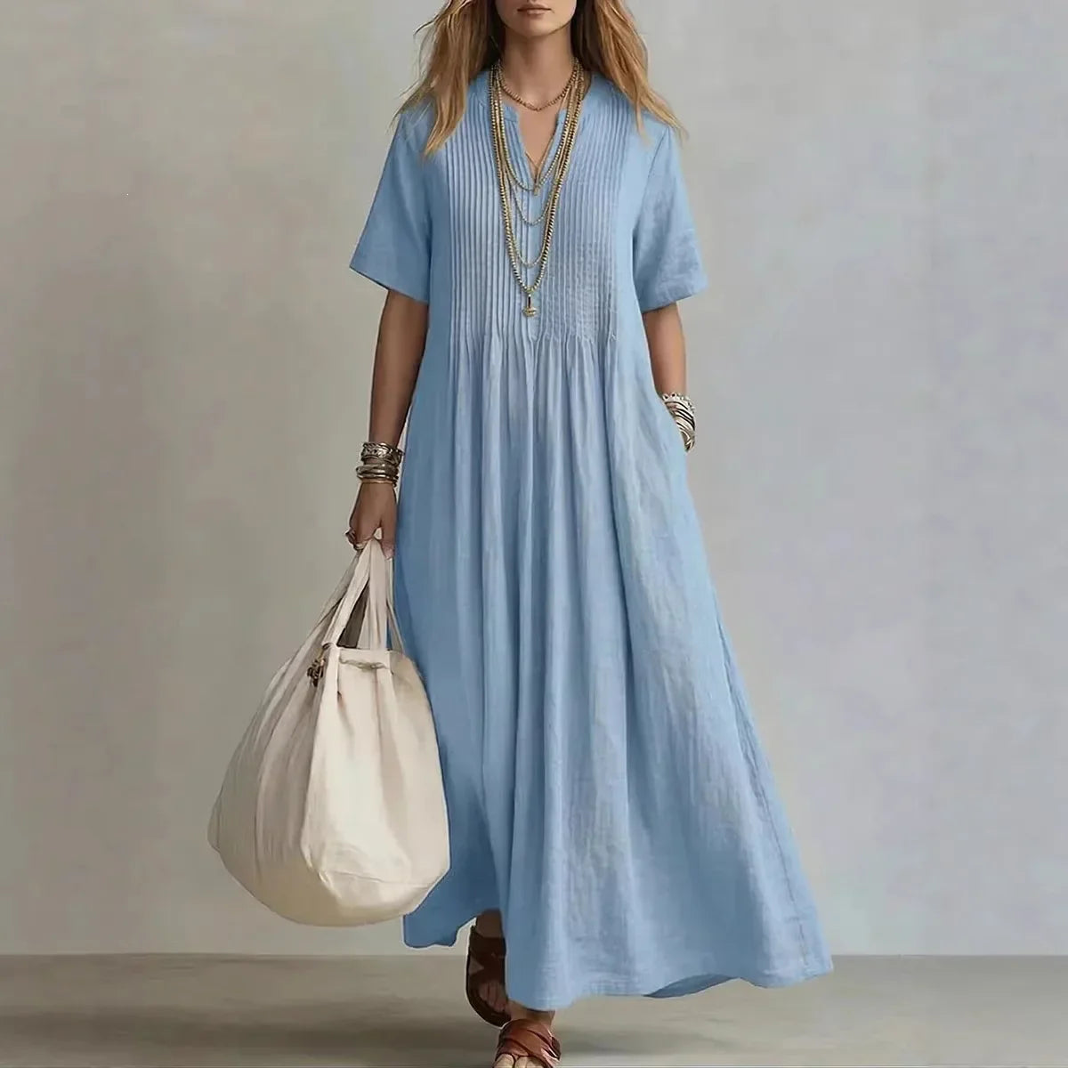 Woman wearing a light blue dress holding a beige bag against a neutral background