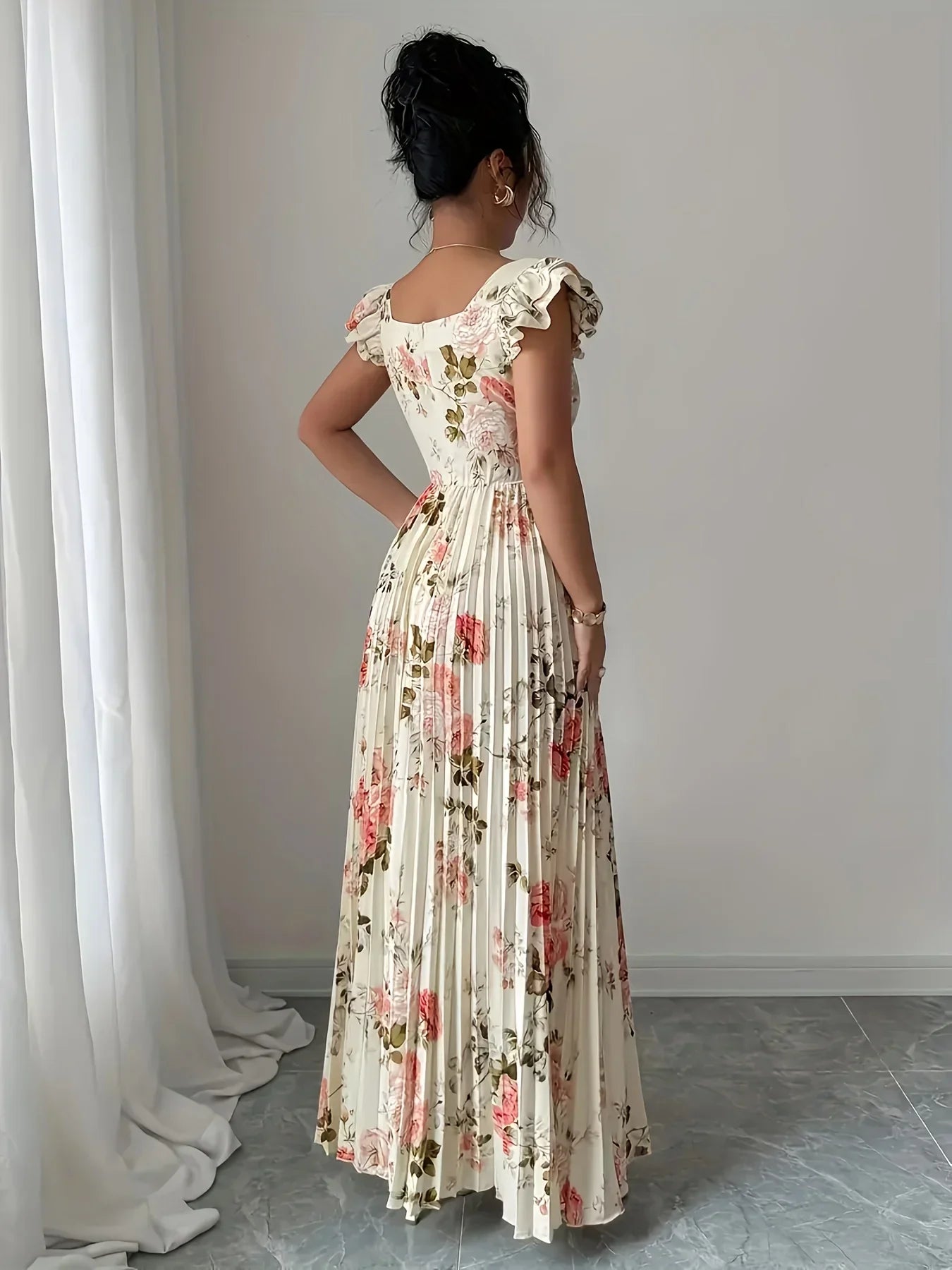 Woman wearing a floral dress standing in a room with white curtains.