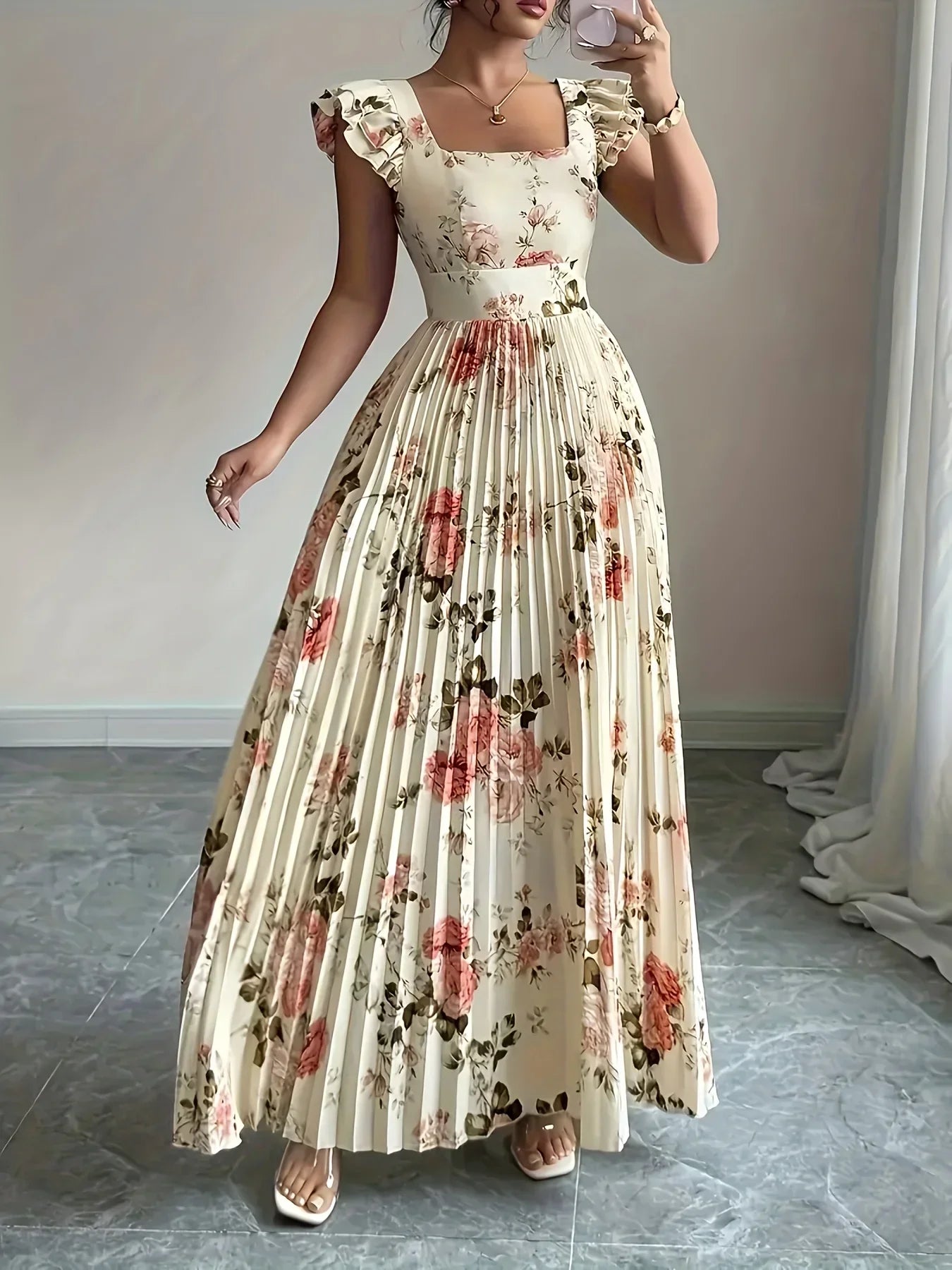Woman wearing a floral dress taking a mirror selfie in a room with light-colored walls.