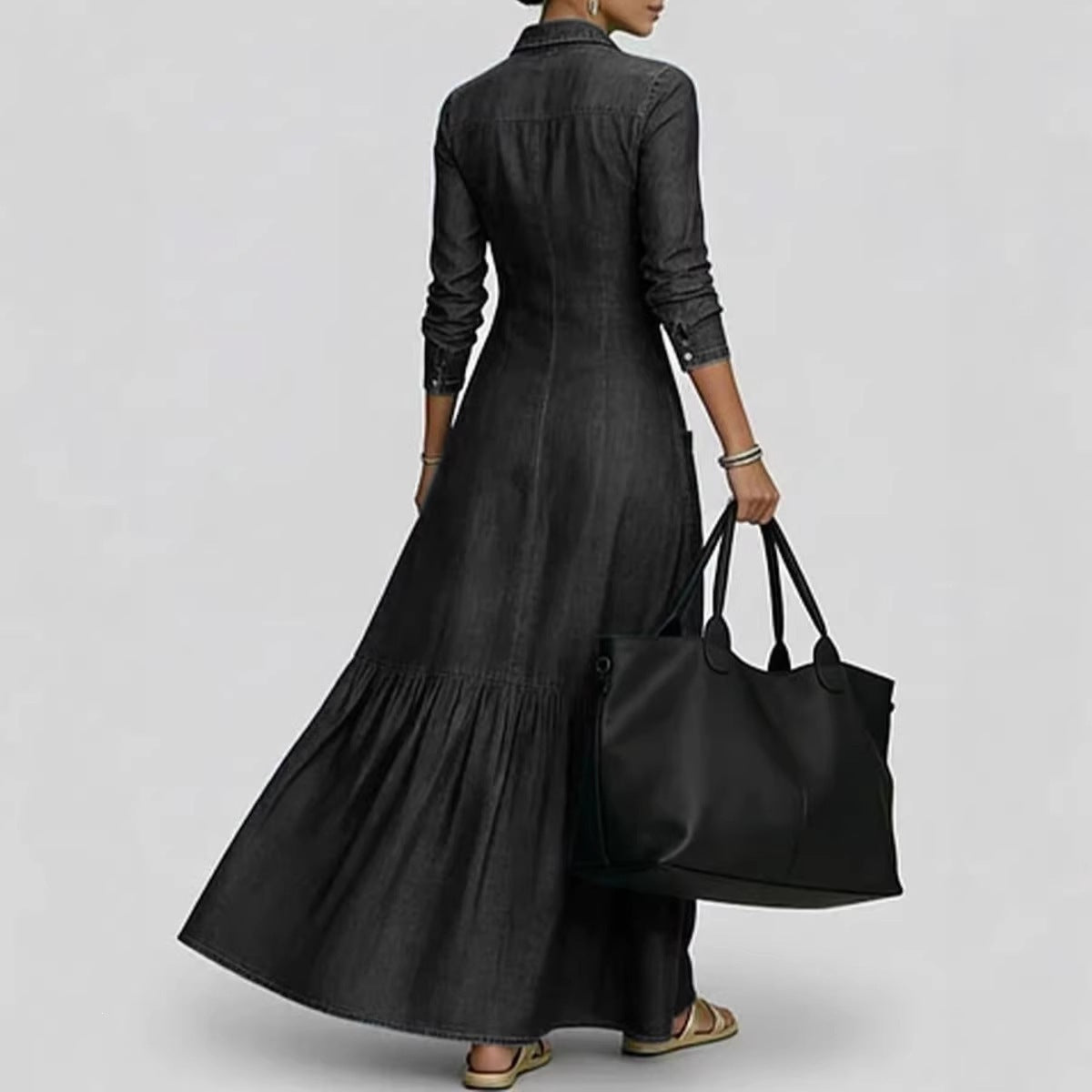 Person wearing a long black dress holding a matching black bag on a light gray background