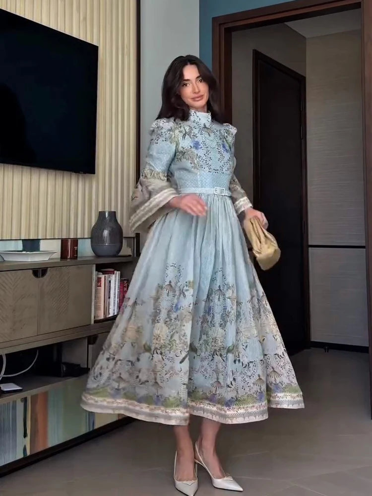 Woman in a light blue floral dress standing in a room with a television and bookshelf.