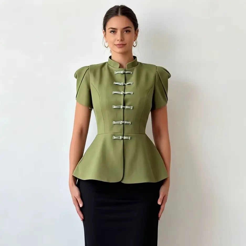 A woman modeling a sage green short-sleeve peplum top with silver decorative frog closures, paired with a black skirt, against a plain light gray background.