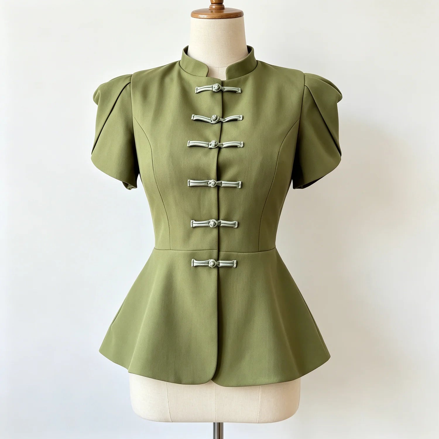 An olive green short-sleeve peplum top with silver metal toggle closures down the front, displayed on a cream-colored dress form mannequin against a plain white background.