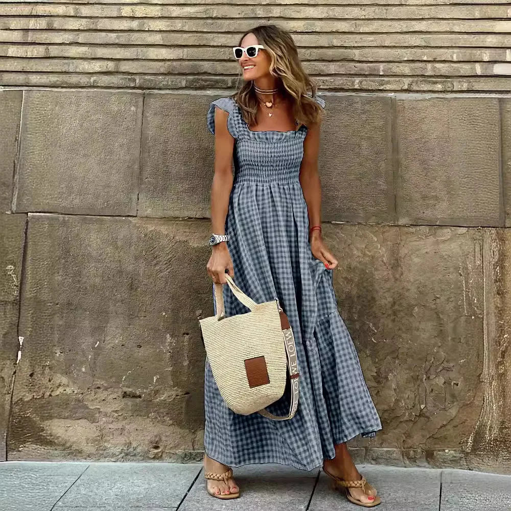 Woman in a blue checkered dress holding a straw bag against a stone wall.