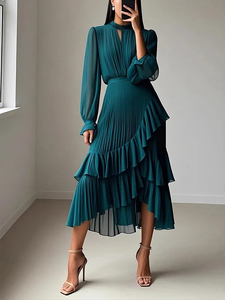 Woman wearing a teal dress with ruffled layers in a minimalistic room.
