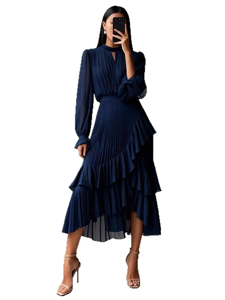A woman modeling a dark navy blue pleated midi dress with long sleeves, a keyhole neckline, and a tiered ruffled skirt, shown against a plain white background.
