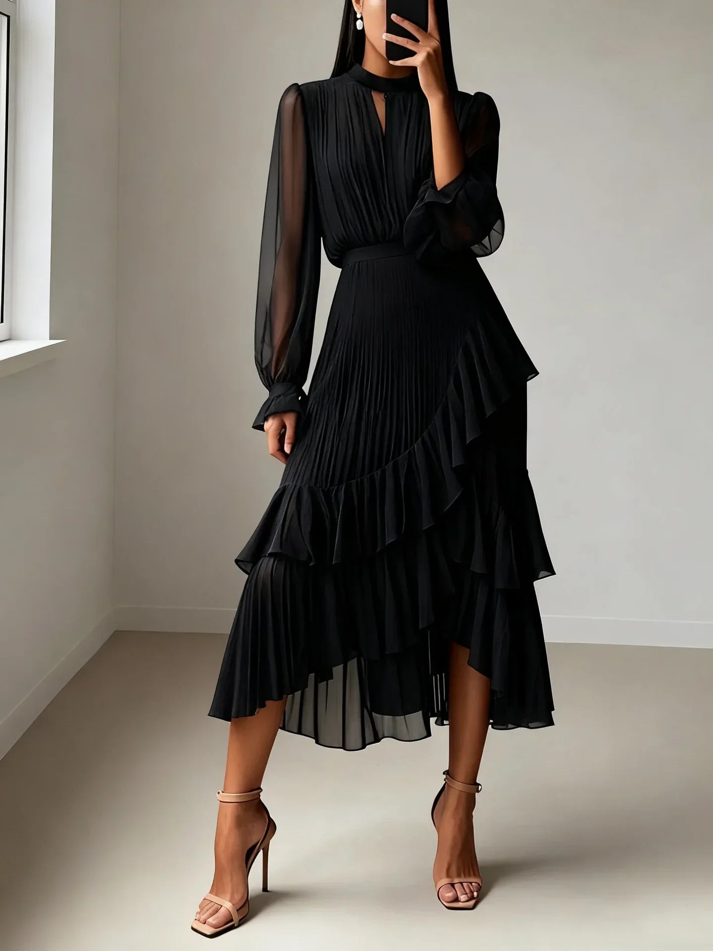 Woman wearing a black dress with sheer sleeves in a minimalistic room.