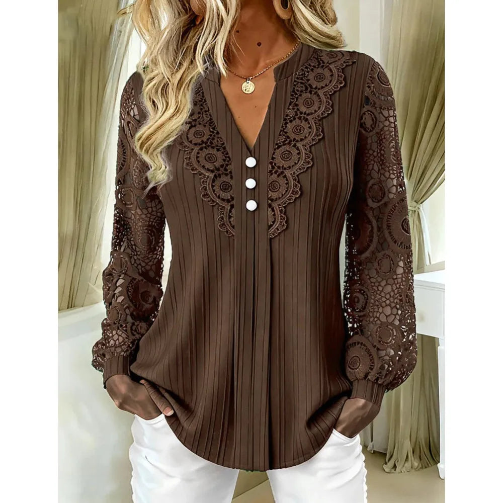 A woman wearing a brown pleated blouse with lace sleeves and a lace V-neckline with white buttons, paired with white pants, in an indoor setting.