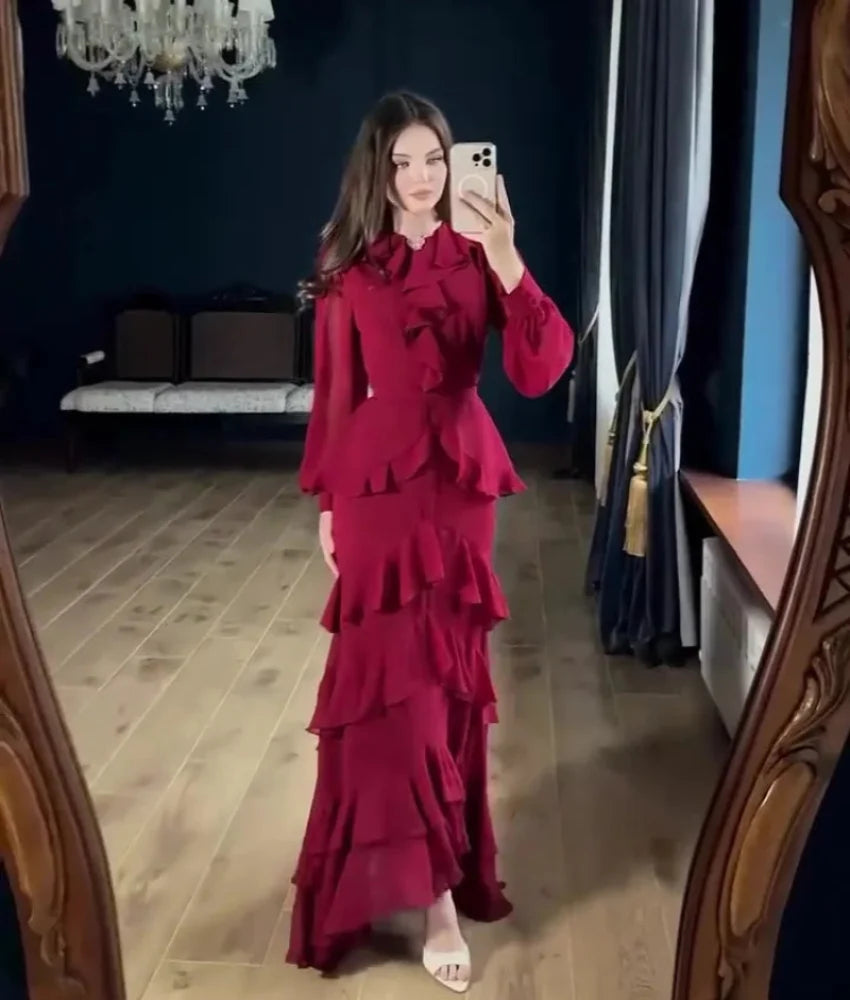 Woman taking a mirror selfie wearing a red ruffled dress in a room with dark walls and wooden floor.