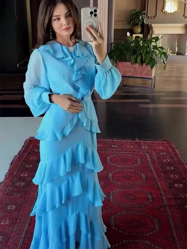 Woman taking a mirror selfie wearing a blue ruffled dress in a room with a red patterned rug.