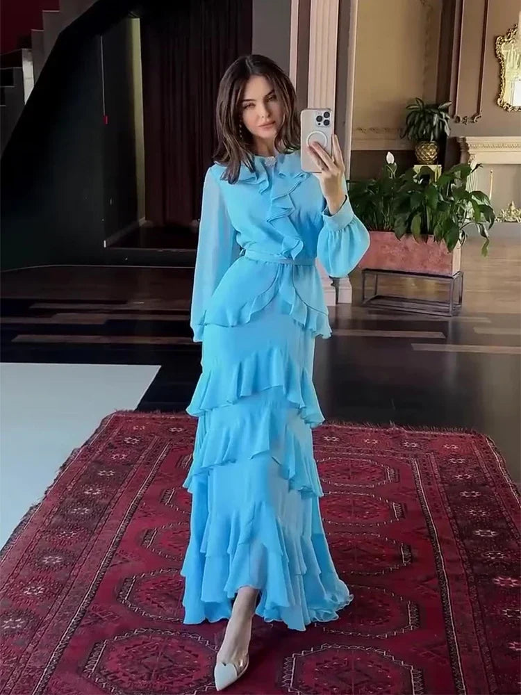 Woman in a blue dress taking a mirror selfie on a red patterned rug.