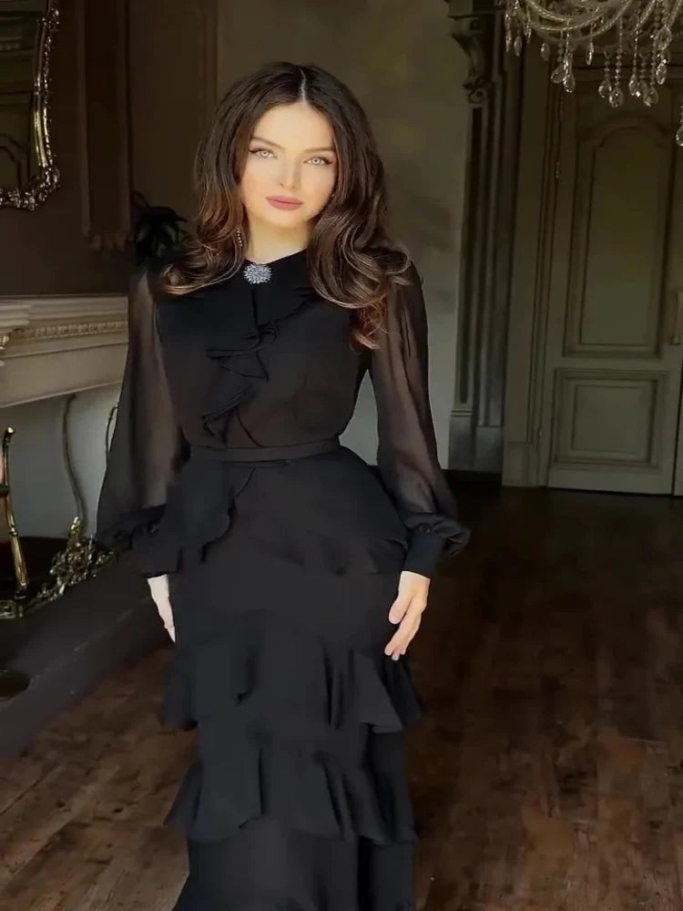 Woman in a black dress standing in an elegant room with a chandelier.