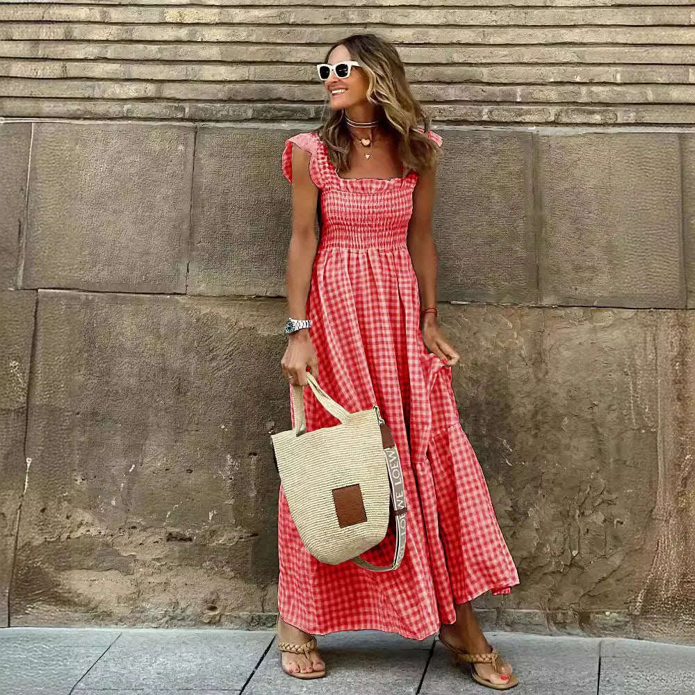 Woman in a red checkered dress holding a straw bag against a stone wall.