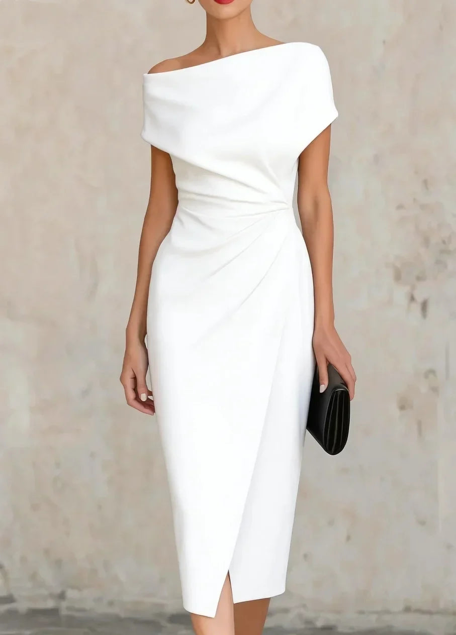 A woman wearing a white off-the-shoulder midi dress with a gathered waist and wrap-style skirt, holding a black clutch against a textured beige wall.