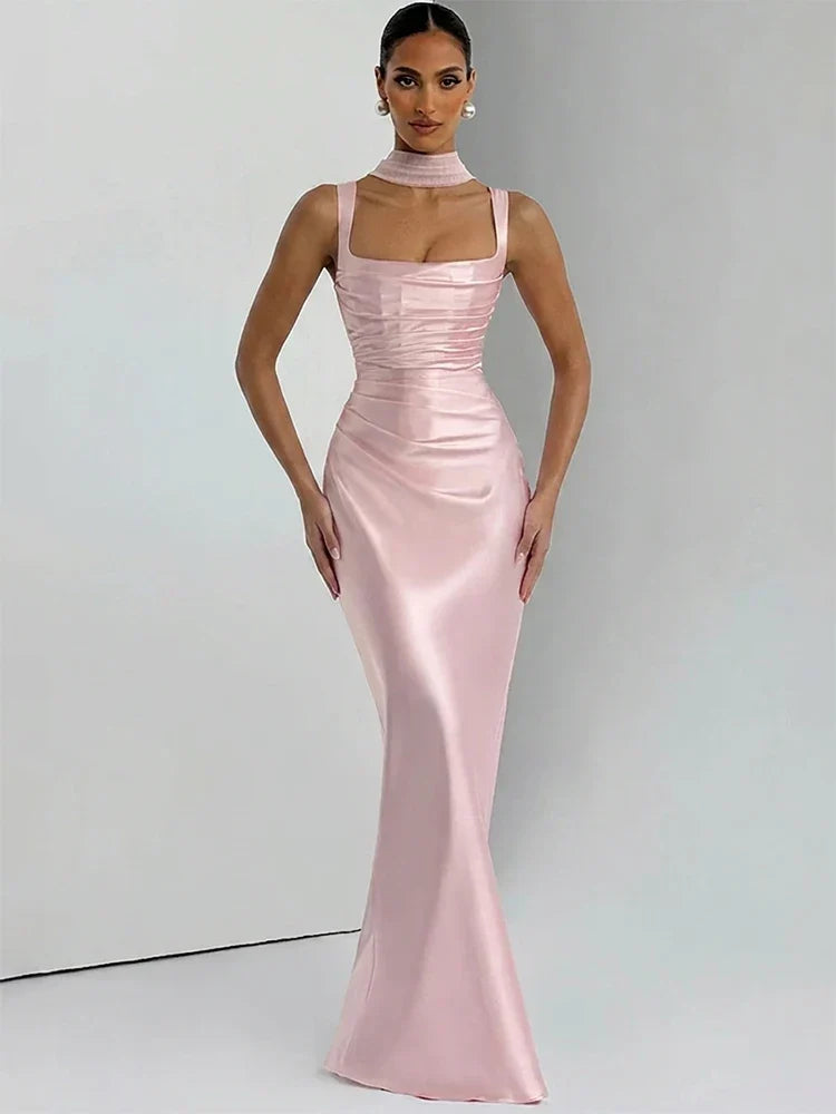 A woman modeling a floor-length light pink satin gown with a high neck, square neckline, ruched bodice, and fitted silhouette against a plain light gray studio background.