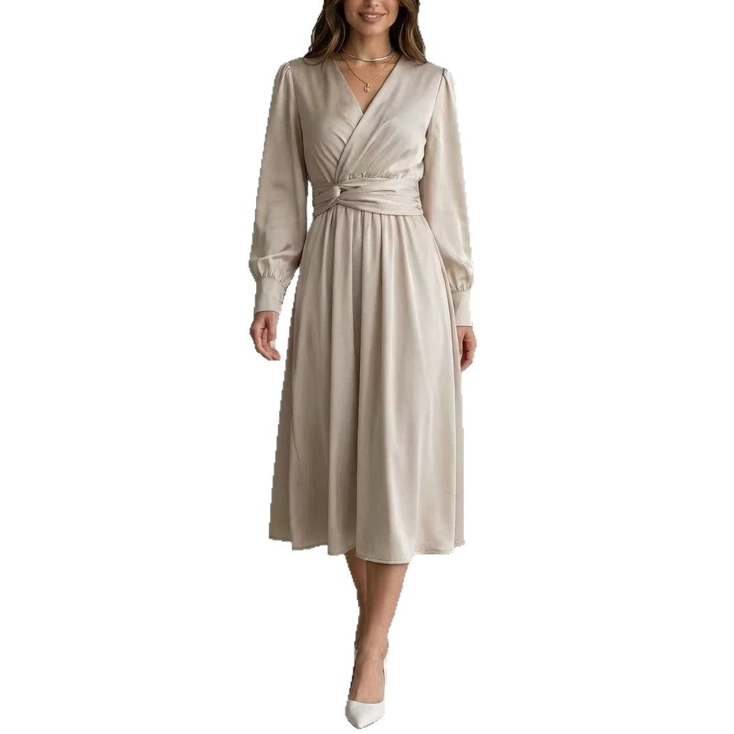 A woman modeling a long-sleeve wrap-style midi dress in a light beige or champagne color, featuring a self-tie waist belt and a V-neckline, set against a plain white background.