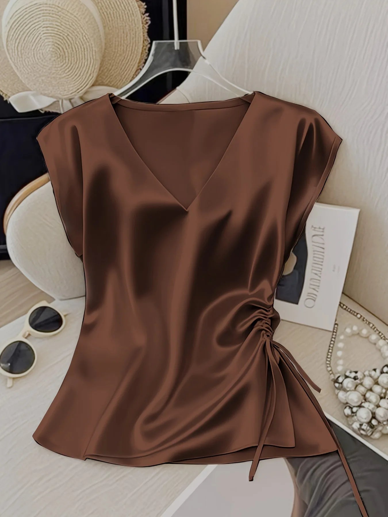 Brown satin top on a surface with accessories in the background