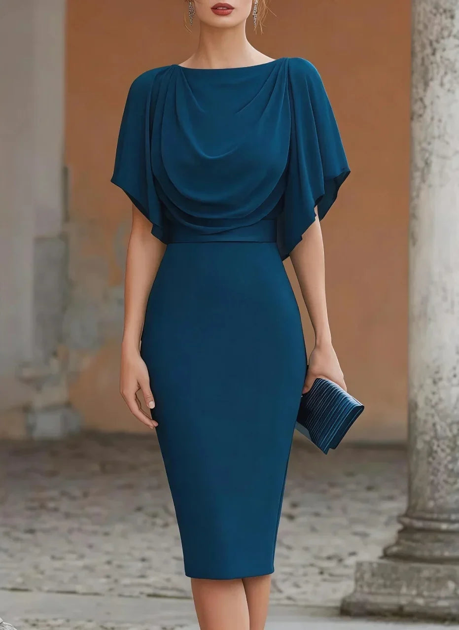 A woman wearing a teal blue knee-length dress with a draped neckline and short flutter sleeves, holding a matching pleated clutch in an outdoor architectural setting.