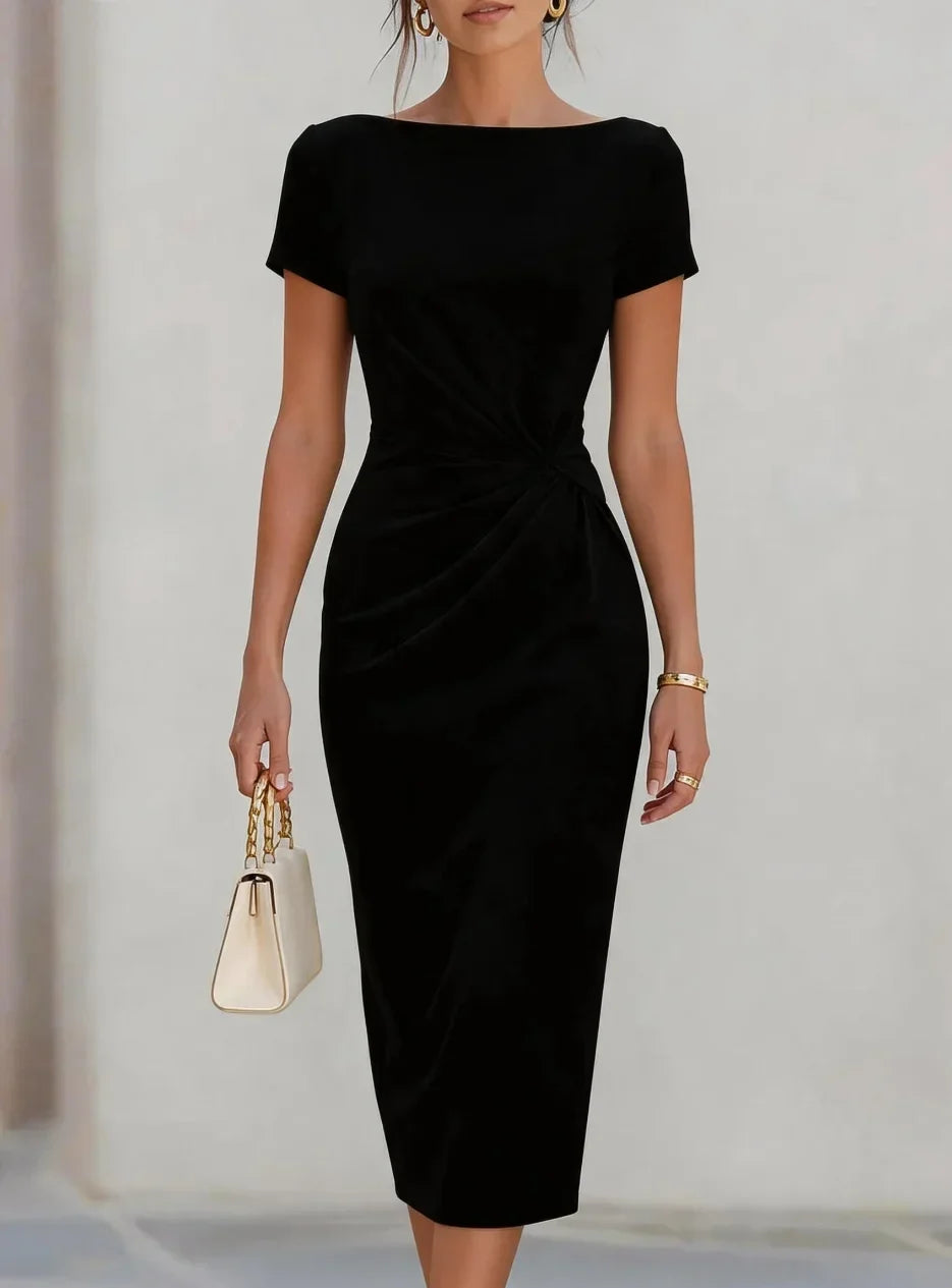 A woman wearing a black short-sleeve midi dress with a twisted waist detail, holding a small cream handbag with gold hardware.