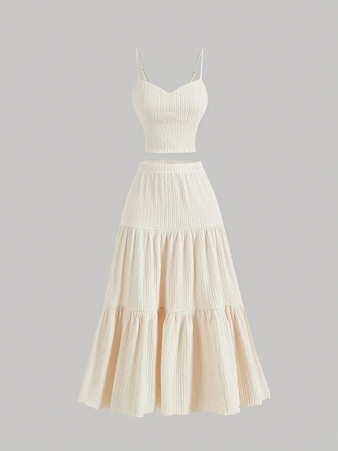 An off-white two-piece set featuring a ribbed crop top with spaghetti straps and a matching tiered maxi skirt, displayed on a neutral gray background.