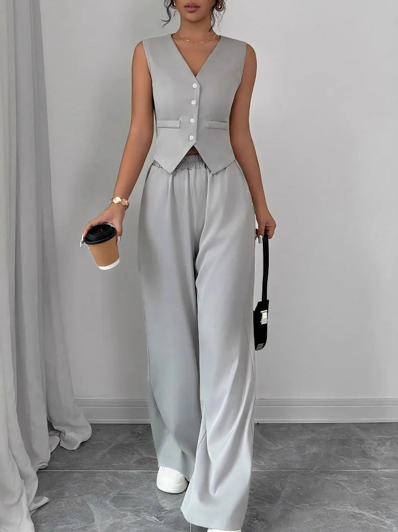 Person wearing a gray vest and wide-leg pants holding a coffee cup and black handbag.