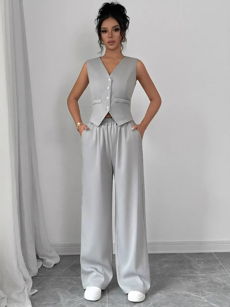 Woman wearing a gray vest and wide-leg pants against a plain background