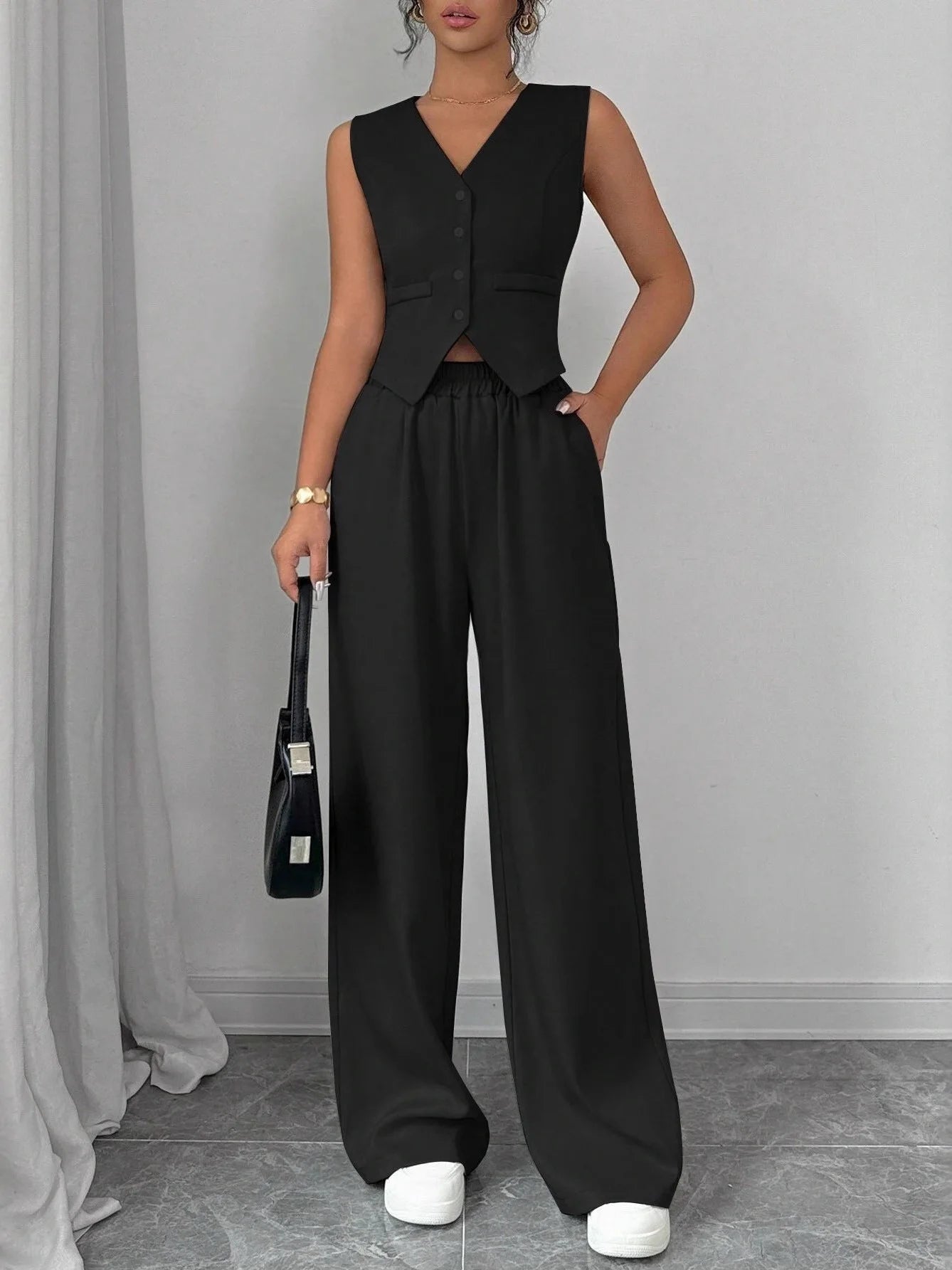 Person wearing a black sleeveless top and wide-leg pants against a gray background