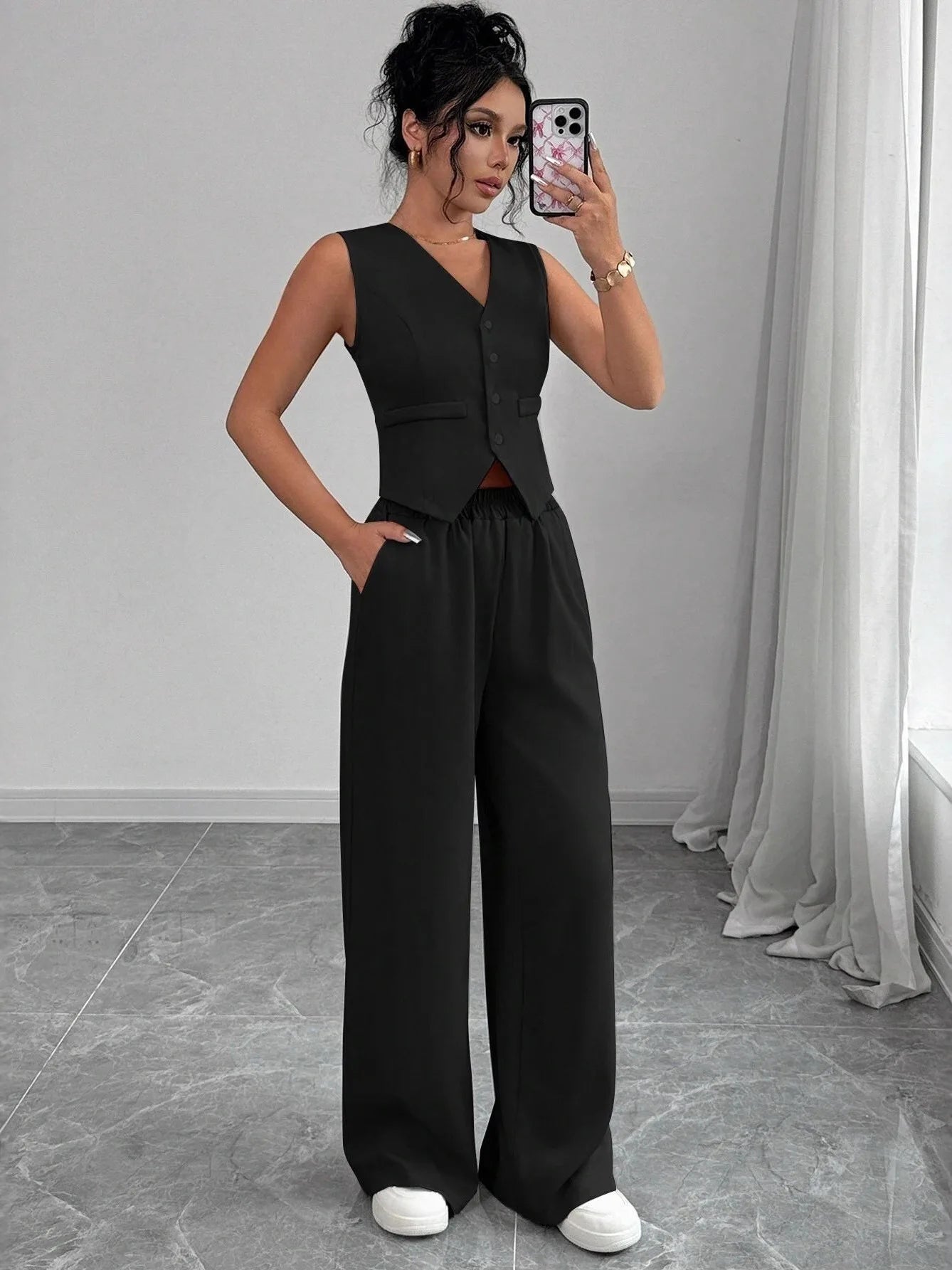Woman wearing a black sleeveless jumpsuit taking a mirror selfie.