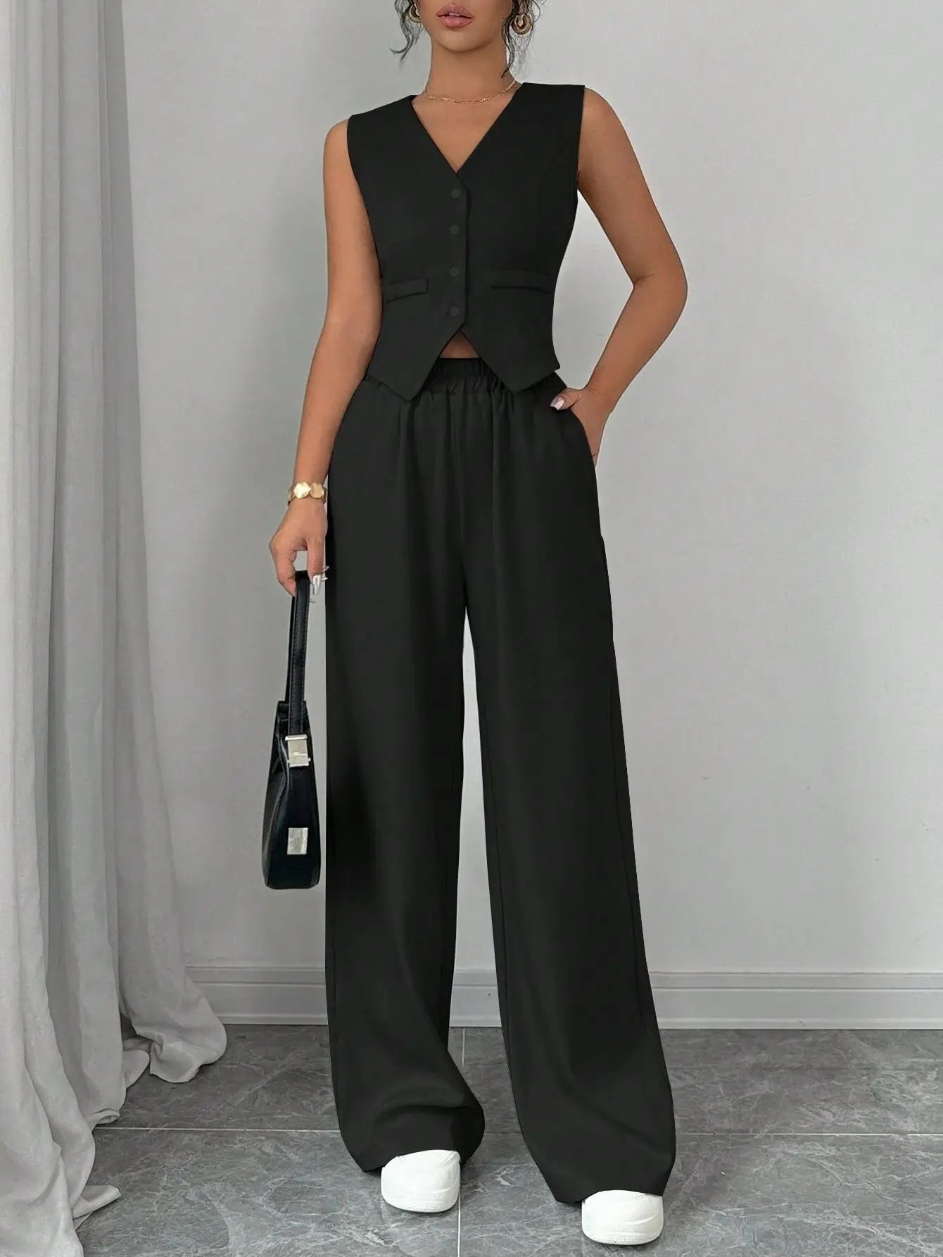Person wearing a black sleeveless top and wide-leg pants against a gray background