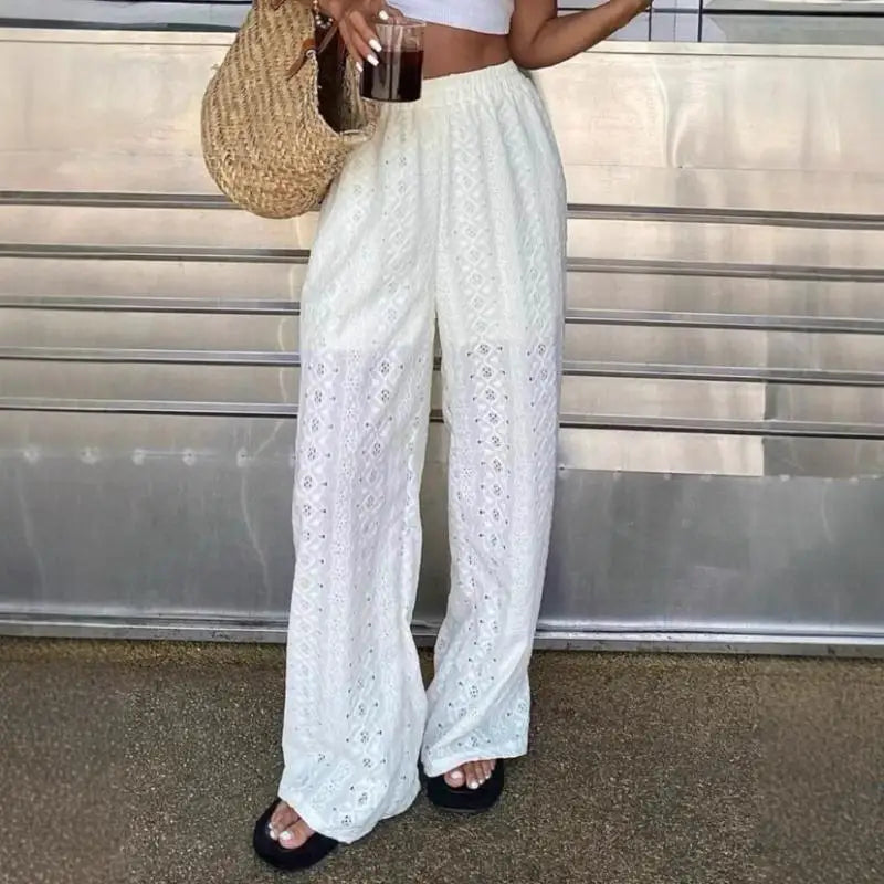 Person wearing white lace pants with a straw bag against a metallic background