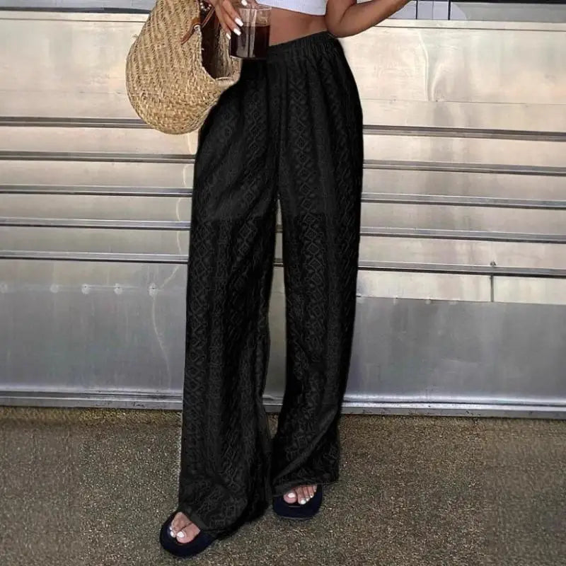 Person wearing black wide-leg pants standing against a metallic wall.