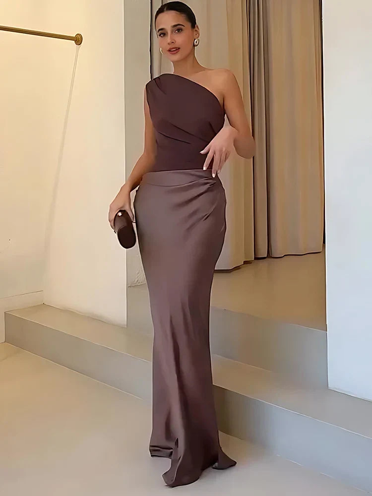 Woman in a one-shoulder brown dress standing on a staircase.