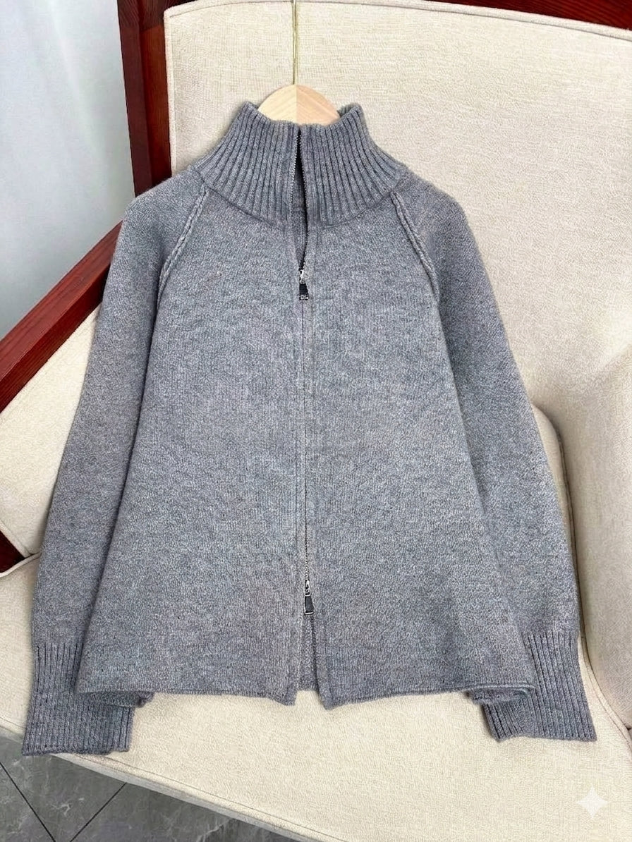 A gray knit zip-up sweater with a mock neck collar, displayed on a beige upholstered chair.